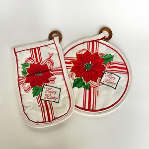 May include: A white oven mitt and round pot holder set with a red poinsettia design and red and white striped ribbon. The text "Happy Holidays" is on a small tag. Both items have wooden hanging loops.