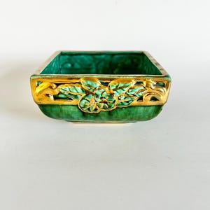 May include: A square, green ceramic dish with a gold floral design around the rim. The dish has a glossy finish and a textured interior. The gold trim adds a touch of elegance to this decorative piece.