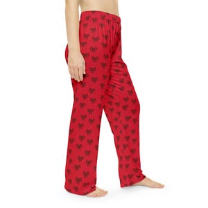 May include: Red lounge pants featuring a repeating pattern of small black bows. The pants have a high elastic waistband and a loose, straight-leg fit, extending from the waist down to the ankles, showcasing a consistent bow print throughout.