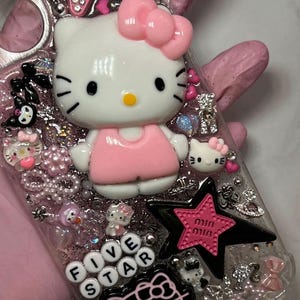 May include: A clear phone case decorated with pink, white and black Hello Kitty characters, rhinestones and glitter. The case also features a pink star with the text "mini mini" and the words "Five Star" in white letters.