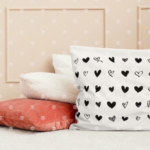 May include: A white cushion with a black and white heart pattern. The cushion is sitting on top of a red cushion and a white cushion. The cushions are on a white surface.