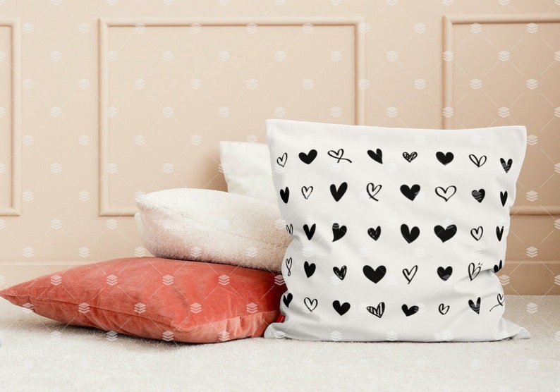 May include: A white cushion with a black and white heart pattern. The cushion is sitting on top of a red cushion and a white cushion. The cushions are on a white surface.