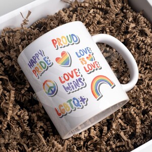以下が含まれることがあります： 虹のデザインと「Happy Pride」、「Proud」、「Love is Love」、「Love Wins」、「LGBTQ+」の文字が書かれた白いセラミックマグカップ。