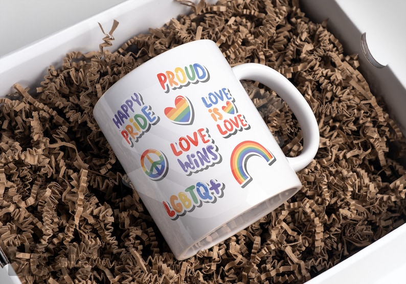 以下が含まれることがあります： 虹のデザインと「Happy Pride」、「Proud」、「Love is Love」、「Love Wins」、「LGBTQ+」の文字が書かれた白いセラミックマグカップ。