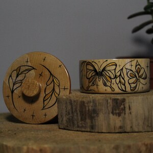 May include: Two wooden boxes with butterfly designs. The lid of the box on the left has a leaf design with gold accents. The box on the right has a butterfly design with gold accents.