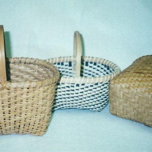 May include: Three woven baskets with handles. The basket on the left is a light brown color, the basket in the middle is white with black stripes, and the basket on the right is a darker brown color.
