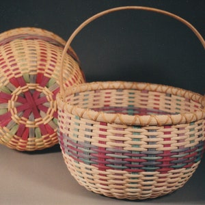 May include: Two woven baskets with a colorful pattern of pink, green, and blue. The basket on the left is closed and the basket on the right has a handle and is open.