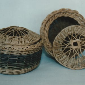 Puede incluir: Dos cestas de mimbre tejidas, una con una banda negra alrededor del medio y la otra con una tapa. Ambas cestas están hechas de materiales naturales y tienen un aspecto rústico y hecho a mano.