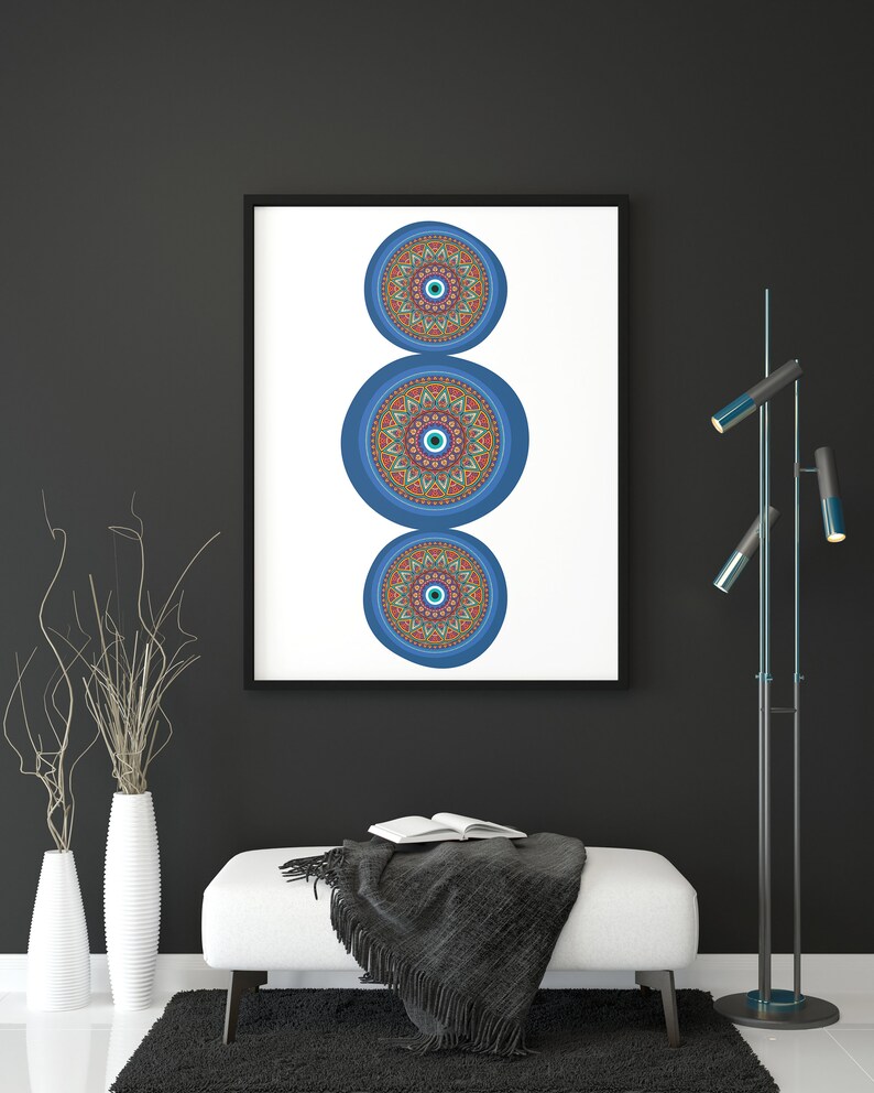 May include: A framed print featuring three blue and orange mandala designs with an evil eye motif. The print is hanging on a black wall above a white ottoman with a black throw blanket.