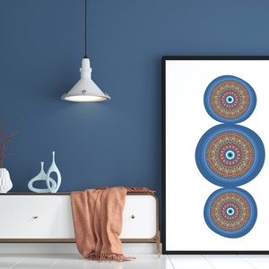 May include: A framed print featuring three blue and red mandala designs with an evil eye in the centre of each. The print is hanging on a blue wall above a white dresser with a brown throw blanket.