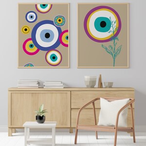 May include: Two framed prints with a beige background. The print on the left features a pattern of blue, teal, yellow, pink, and white circles with an eye design. The print on the right features a single large blue, teal, yellow, and purple circle with an eye design and a green plant stem.