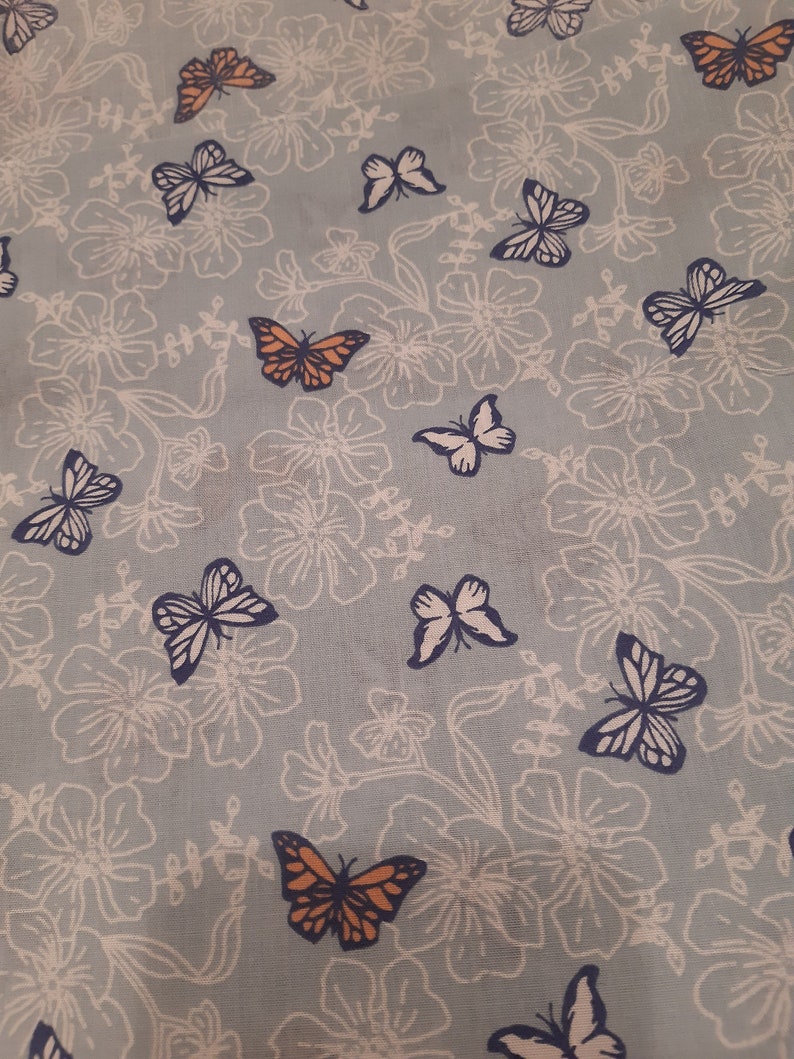 May include: A light blue fabric with a white floral pattern and orange and blue butterflies.
