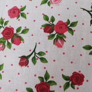 May include: White fabric with a repeating pattern of pink roses and small pink dots. The roses have green leaves and stems.