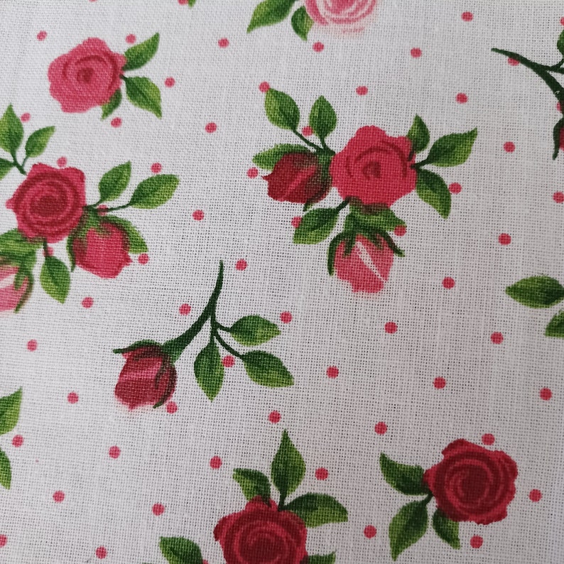 May include: White fabric with a repeating pattern of pink roses and small pink dots. The roses have green leaves and stems.