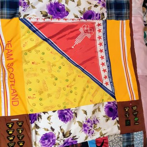 Puede incluir: Una colcha de retazos hecha de varias telas, incluyendo patrones florales, cuadros y colores s&oacute;lidos. La colcha presenta un panel amarillo con el texto "TEAM SCOTLAND" y un panel rojo con el texto "MOSKVA 1980 МОСКВА 1980 MOSKVA 1980 МОСКВА 1980 MOKY".
