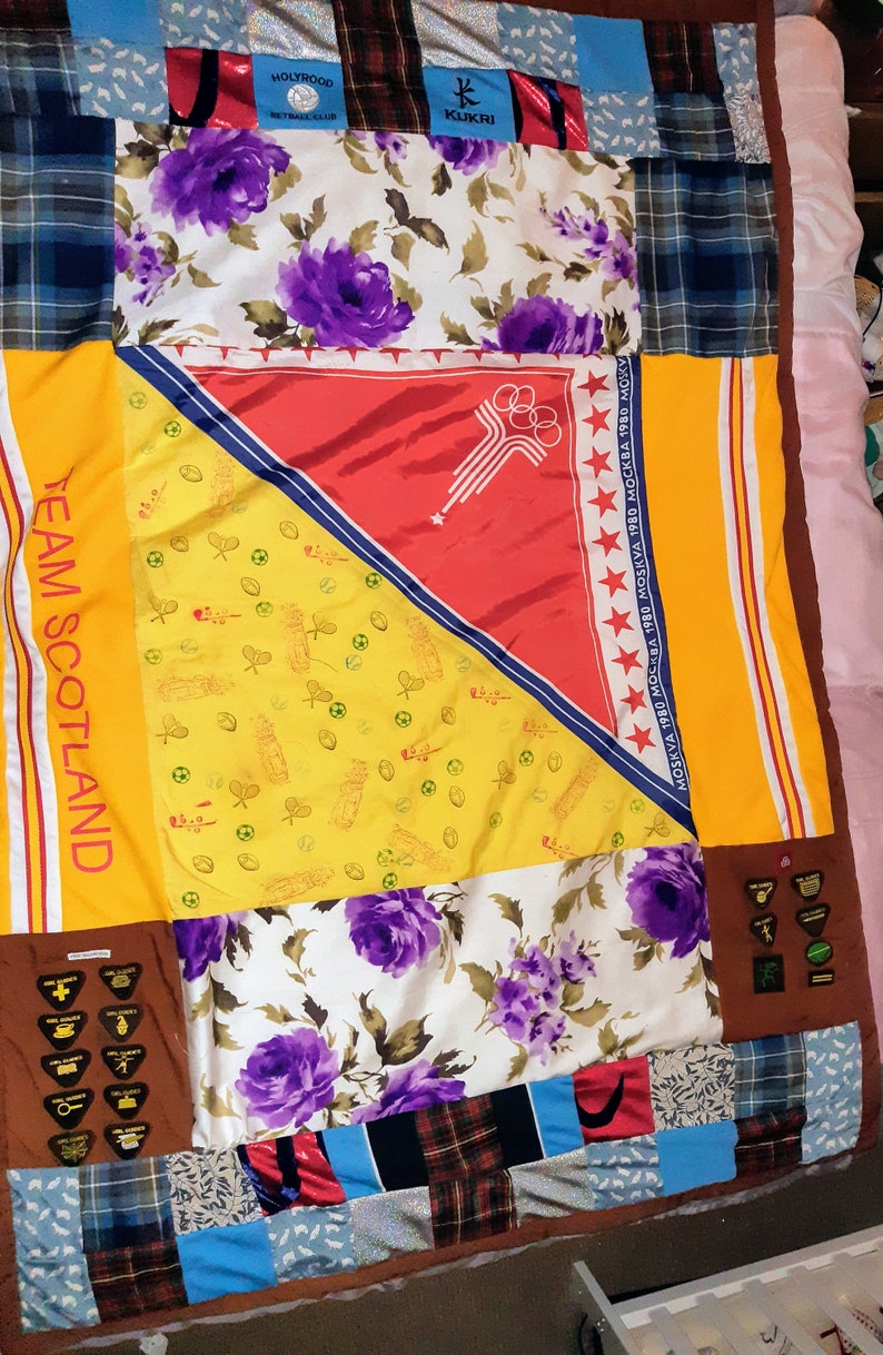 Puede incluir: Una colcha de retazos hecha de varias telas, incluyendo patrones florales, cuadros y colores s&oacute;lidos. La colcha presenta un panel amarillo con el texto "TEAM SCOTLAND" y un panel rojo con el texto "MOSKVA 1980 МОСКВА 1980 MOSKVA 1980 МОСКВА 1980 MOKY".