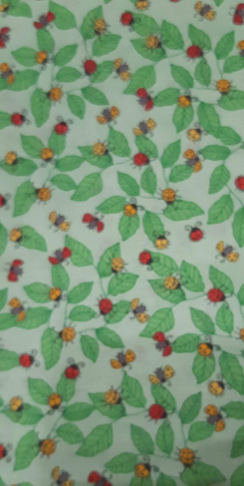 May include: A green fabric with a repeating pattern of red ladybirds and yellow bumblebees on green leaves.