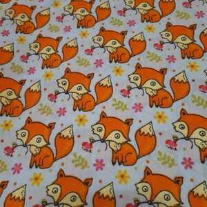 May include: A white fabric with a repeating pattern of orange foxes holding a flower. The foxes have black eyes and a black nose. The flowers are pink, yellow, and green.