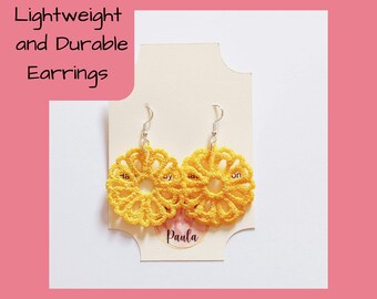 Puede incluir: Un par de pendientes de crochet amarillo con ganchos plateados. Los pendientes son ligeros y duraderos. Los pendientes están en una tarjeta blanca con el texto "Paula" escrito en ella.