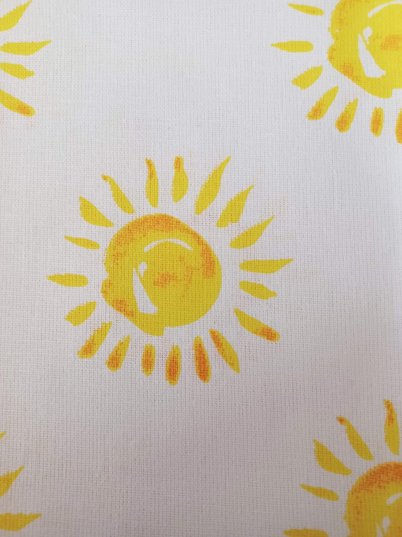May include: White fabric with a repeating pattern of yellow suns. Each sun has a yellow centre and orange rays.