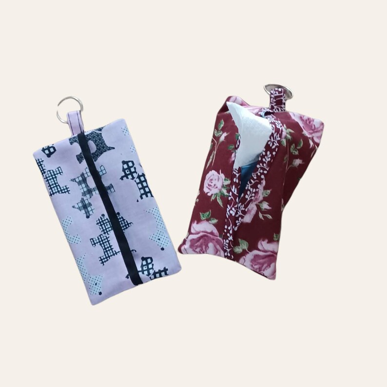 May include: Two fabric tissue holders with key rings. One is pink with a black and white pattern of dogs. The other is burgundy with a floral pattern.