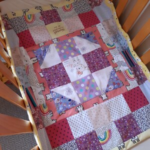 Puede incluir: Una colcha de beb&eacute; de retazos en colores rosa, morado y amarillo. La colcha presenta una variedad de patrones, incluyendo lunares, rayas e estampados florales. La colcha est&aacute; hecha de tela suave y c&oacute;moda, perfecta para acurrucarse con un peque&ntilde;o. La colcha tiene un mensaje personalizado que dice "Hannah, te queremos mucho, 01.08.2019".