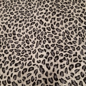 May include: A white fabric with a black and grey leopard print pattern.