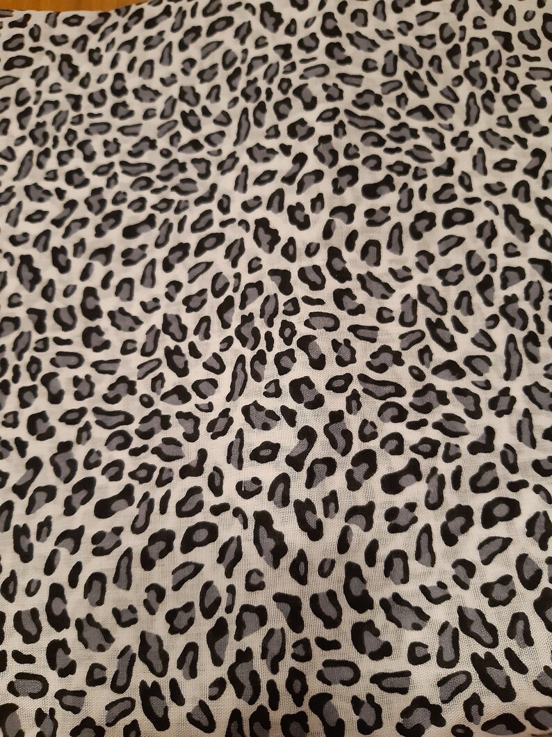 May include: A white fabric with a black and grey leopard print pattern.