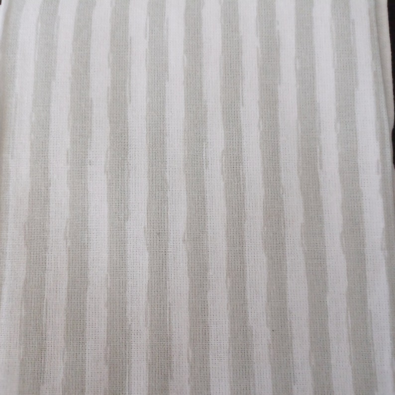 May include: White fabric with thin, grey stripes. The fabric has a woven texture.
