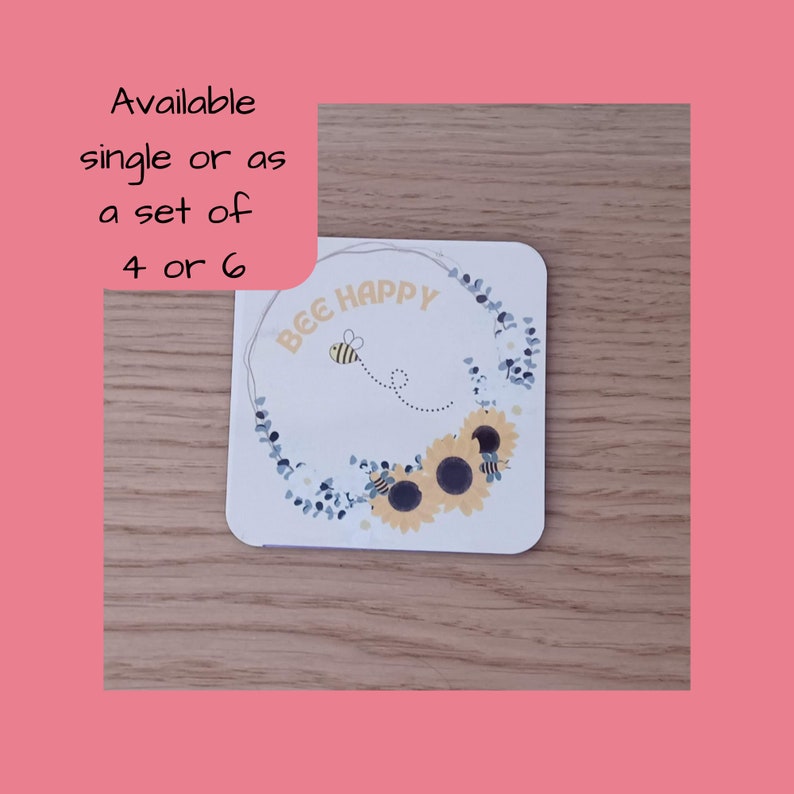 K&ouml;nnte beinhalten: Wei&szlig;er Untersetzer mit einem blauen und gelben Blumendesign und dem Text "Bee Happy".