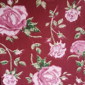 May include: A red fabric with a repeating pattern of pink roses and green leaves.