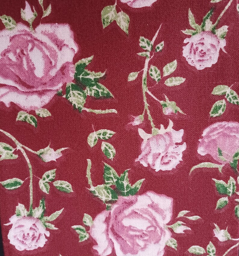May include: A red fabric with a repeating pattern of pink roses and green leaves.