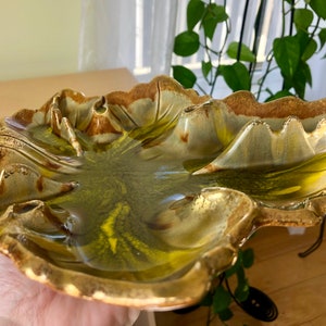 May include: A ceramic leaf-shaped dish with a glossy finish. The dish features a blend of green, brown, and gold tones, with a textured surface and a scalloped edge. The dish is designed to resemble a leaf.