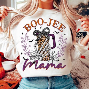 May include: White sweatshirt with a purple and orange graphic of a skeleton hand holding a leopard print coffee cup with a bow. The text "BOO-JEE mama" is printed on the sweatshirt.