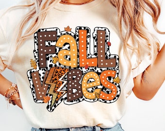May include: A white t-shirt with a graphic design that says "Fall Vibes" in brown, orange, and black letters with a leopard print and polka dot pattern.