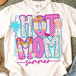 Puede incluir: Camiseta color crema con un gr&aacute;fico colorido que dice "HOT MOM summer". El dise&ntilde;o presenta una palmera, flores, un sol y una rodaja de sand&iacute;a. Las letras son rosas, negras y blancas.