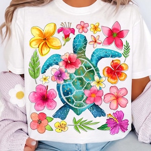 May include: White t-shirt with a watercolor illustration of a green sea turtle surrounded by colorful flowers. The flowers are pink, yellow, orange, and red.