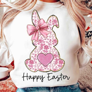 Op de afbeelding: Witte trui met een roze konijn ontwerp en de tekst "Happy Easter". Het konijn heeft een roze strik en een roze hart op zijn borst.
