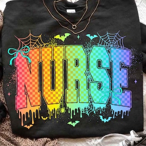May include: Black sweatshirt with the word "NURSE" in large, colorful, checkered letters. The letters transition from pink to yellow to blue. The design includes spiderwebs, bats, and bows, with a Halloween theme.