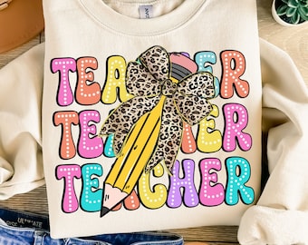 May include: A beige sweatshirt with the word "Teacher" repeated three times in colorful, outlined letters. A large yellow pencil with a leopard print bow is in the center of the design.