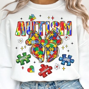 May include: White sweatshirt with a colorful "AUTISM" graphic featuring a puzzle piece bow, hearts, and puzzle pieces with the words "ACCEPT", "LOVE", and "UNDERSTAND".