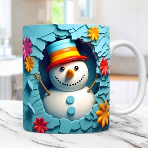 K&ouml;nnte beinhalten: Wei&szlig;e Keramiktasse mit einer 3D-Illustration eines Schneemanns, der einen bunten Hut tr&auml;gt und von einem blauen Rahmen mit Blumen umgeben ist. Der Schneemann hat eine Karottennase und Zweigarme. Die Tasse hat einen wei&szlig;en Henkel.