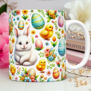 May include: White ceramic mug featuring a colourful Easter design. The design includes a white bunny, yellow chicks, and colourful Easter eggs on a white background.