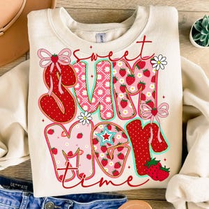Pu&ograve; includere: Una felpa color crema con un design a patchwork delle parole "sweet summer time" in rosso, rosa e bianco. Le lettere sono decorate con fragole, fiori e fiocchi.