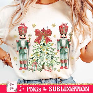 May include: A white t-shirt with a Christmas design featuring two nutcracker soldiers flanking a green Christmas tree with red and gold ornaments. The tree is decorated with a red bow and a gold star.