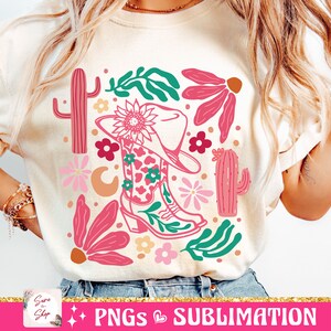 May include: Cream-colored t-shirt featuring a colorful graphic design. The design includes a cowboy boot, a cowboy hat, cacti, flowers, and leaves in shades of pink, green, and orange. The text "PNGS & SUBLIMATION" is at the bottom.