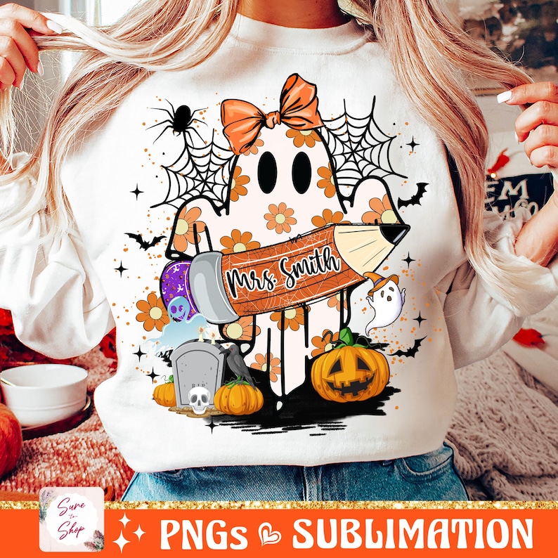 Puede incluir: Una sudadera blanca con un fantasma sosteniendo un l&aacute;piz que dice "Mrs. Smith". El fantasma est&aacute; rodeado de decoraciones de Halloween naranjas y negras, incluyendo calabazas, murci&eacute;lagos y telara&ntilde;as.