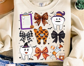 Könnte beinhalten: Ein weißer Pullover mit einem Halloween-Motiv, das eine Zahn mit einer Hexenmütze, eine Klemmbrett mit einem Zahnsymbol und verschiedene Schleifen in schwarz-weißem Karomuster, Leopardenmuster und orange-schwarzem Tupfenmuster zeigt.