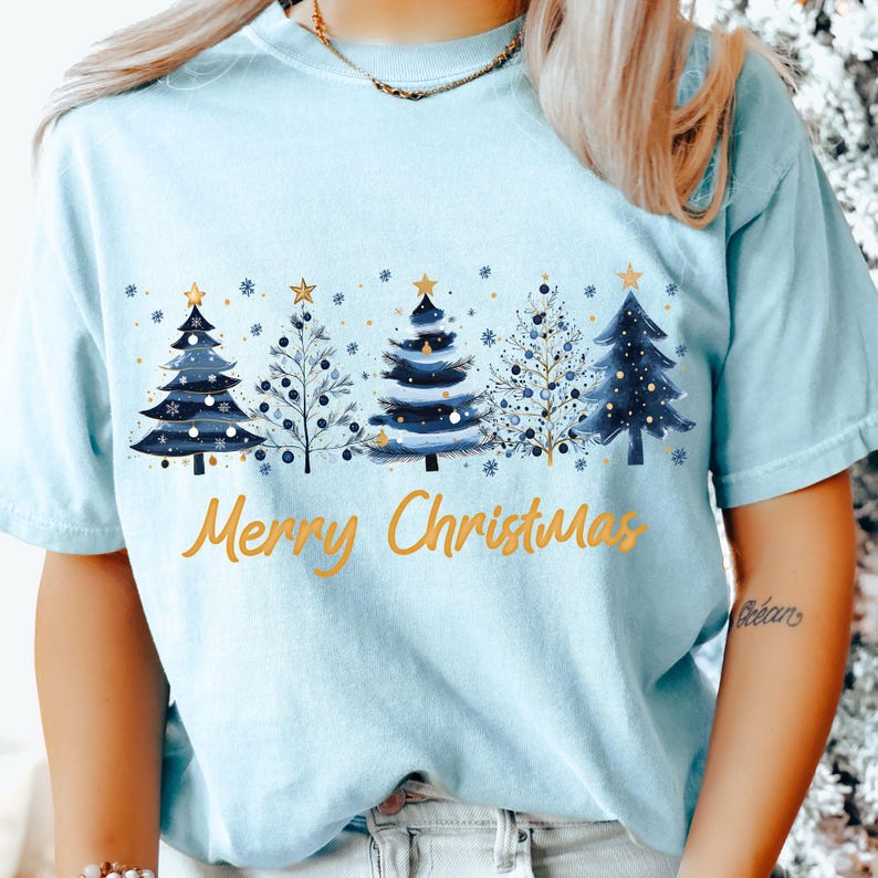 May include: Light blue t-shirt with a graphic of blue Christmas trees with gold accents and the text "Merry Christmas".
