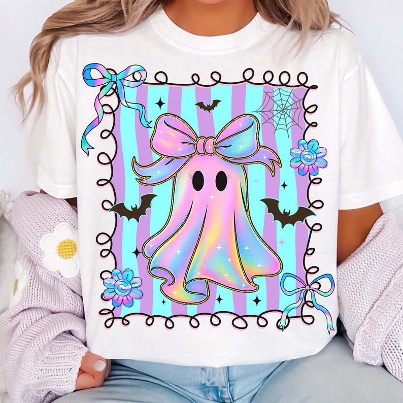 Puede incluir: Camiseta blanca con un dise&ntilde;o de fantasma de arco&iacute;ris pastel. El fantasma tiene un lazo y est&aacute; sobre un fondo a rayas. El dise&ntilde;o incluye murci&eacute;lagos, flores y una telara&ntilde;a, creando un tema de Halloween.